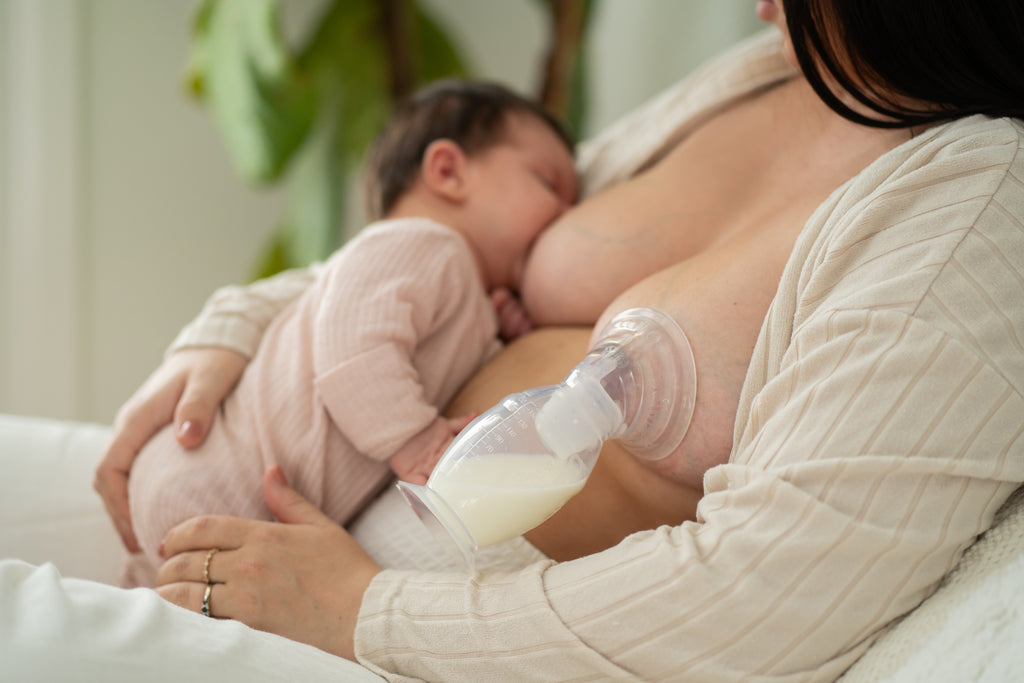 Mother breastfeeding baby while using breast pump to collect milk, cozy home setting