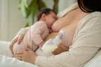 Mother breastfeeding baby while using breast pump to collect milk, cozy home setting