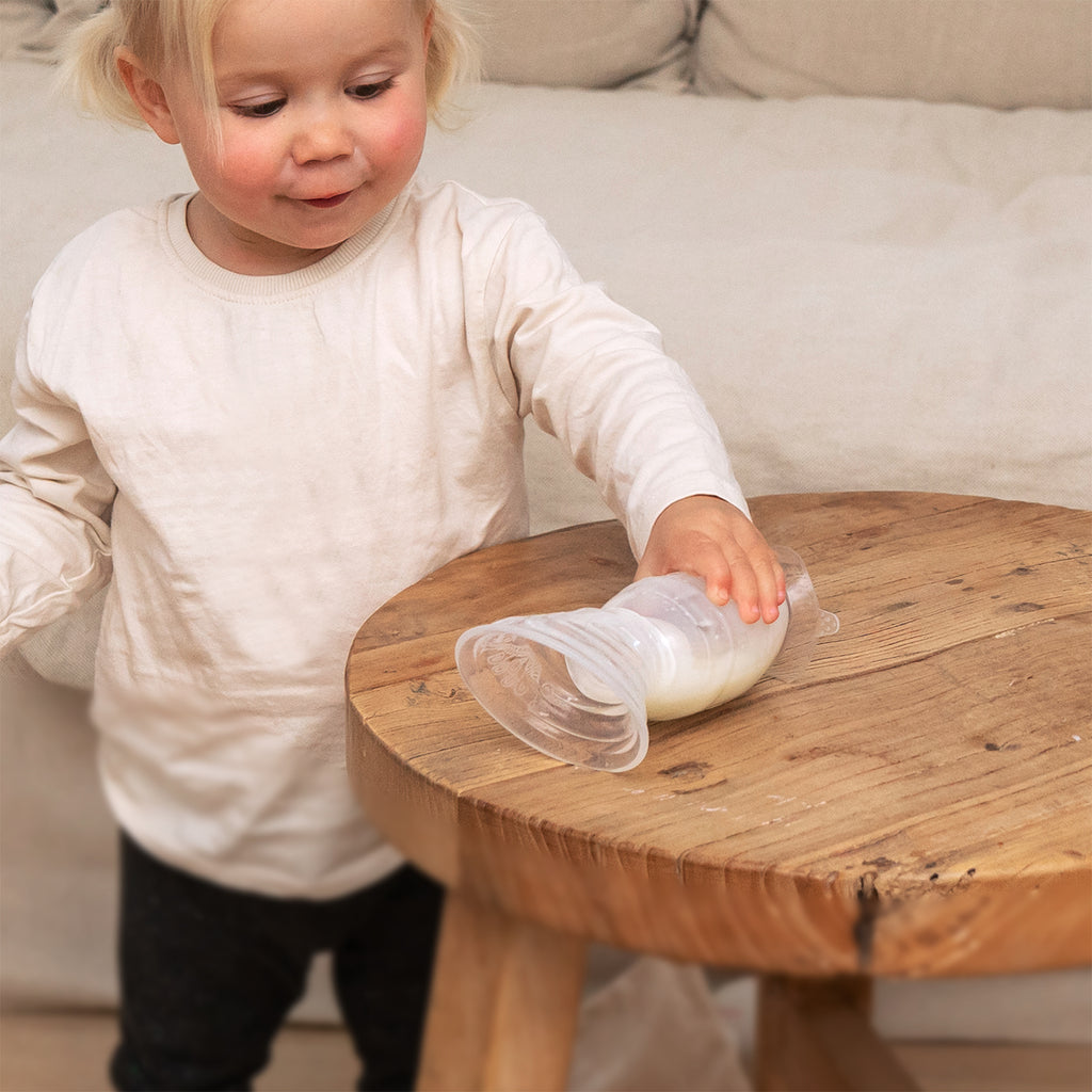 Child holding breast pump with milk on wooden table, eco-friendly baby product